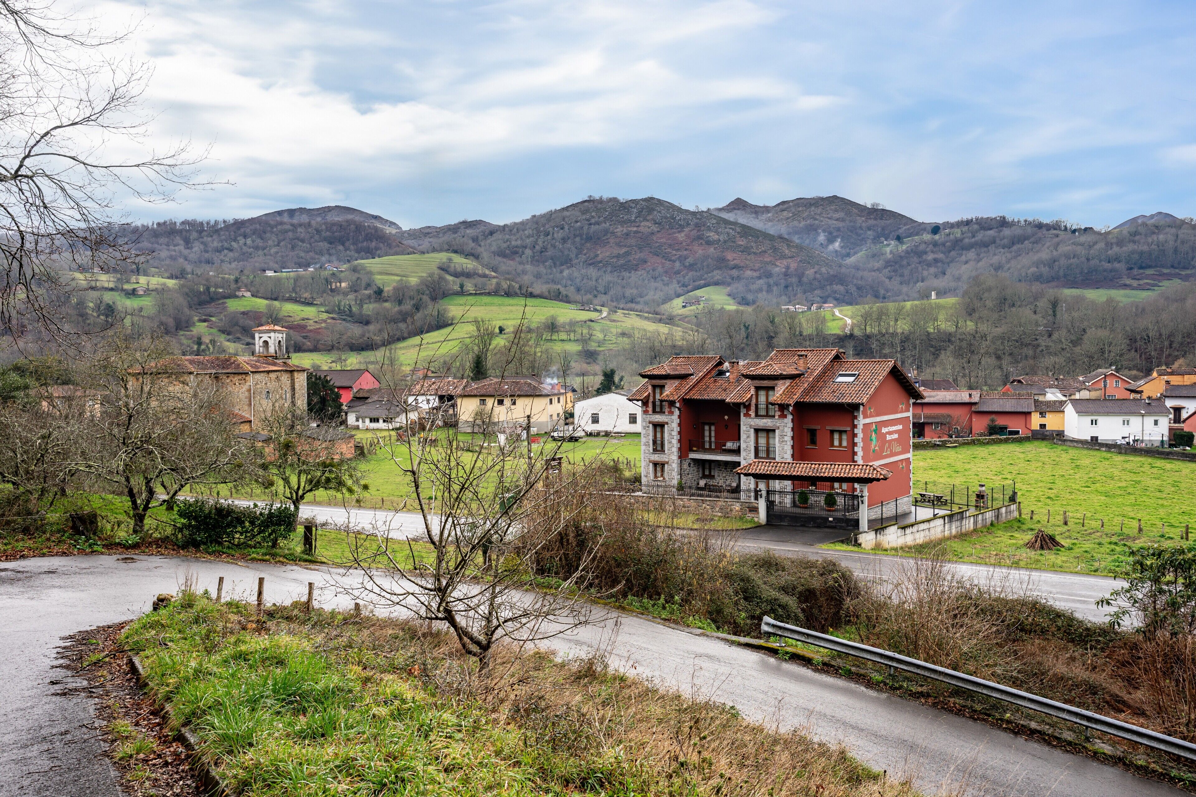 Ein ländliches Dorf mit traditionellen Häusern, einer kurvenreichen Straße und Hügeln im Hintergrund.