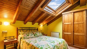 A bedroom with a skylight, wooden ceiling beams, a bed with floral bedding, a nightstand, and a wardrobe. - Apartment 'La Viña 9' with Mountain Views and Wi-Fi (Corao)