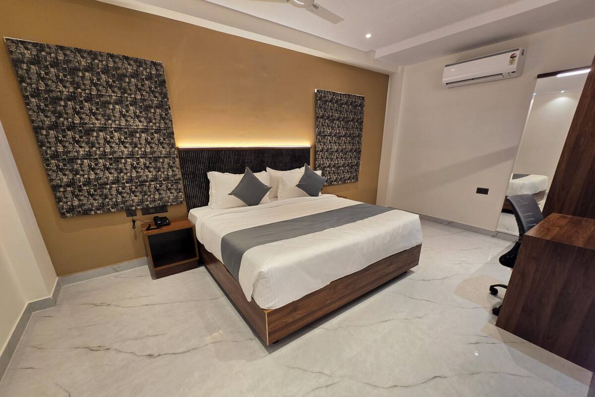 A modern bedroom with a large bed, a nightstand, a wall-mounted air conditioner, and a mirror.