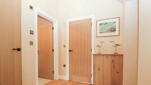 Um corredor com portas de madeira, um quadro com pássaros na parede e uma pequena prateleira com esculturas de aves.