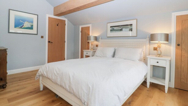Um quarto com uma cama grande, vigas de madeira, duas mesas de cabeceira com luminárias e quadros nas paredes.