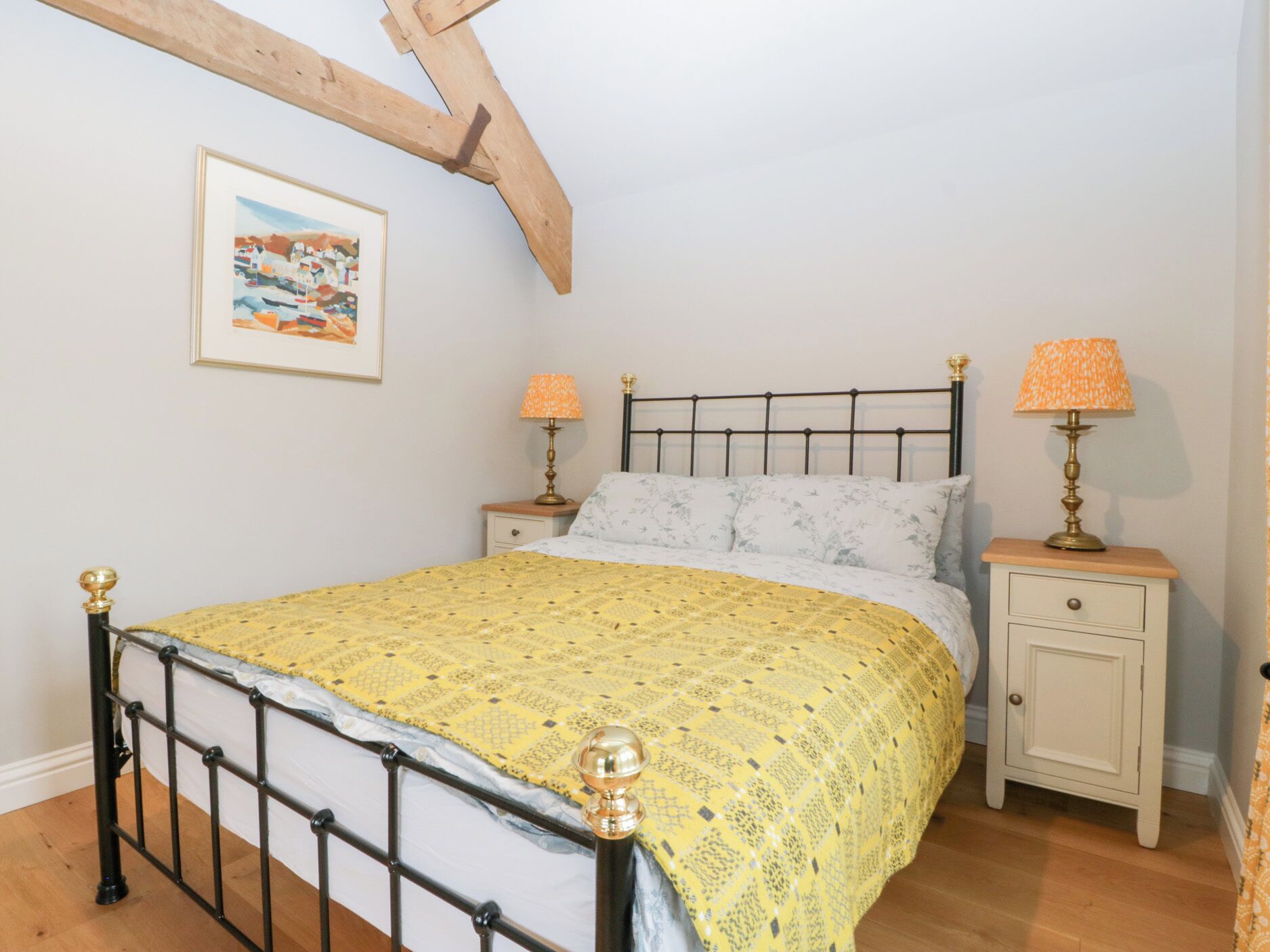 Une chambre à coucher comprenant un lit, deux tables de chevet, une commode, une lampe, un tableau encadré accroché au mur et une structure en poutres apparentes.