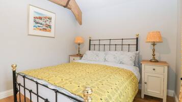 Une chambre à coucher comprenant un lit, deux tables de chevet, une commode, une lampe, un tableau encadré accroché au mur et une structure en poutres apparentes.