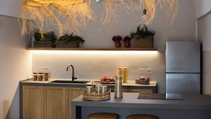 Eine moderne Küche mit integriertem Spülbecken, Holzschränken und einem Edelstahl-Kühlschrank. Auf der Arbeitsfläche stehen Korbwannen und eine Pendelleuchte ist angebracht.