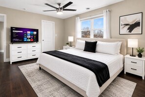 Ein Schlafzimmer mit Bett, Nachttischen, Fernseher, Deckenventilator, Fenster und einem Gemälde.