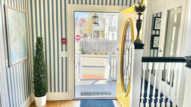 A striped interior wall, a potted plant, a door with a view of the street, and a staircase with white balusters. - The Garden Room at the Lafayette Inn (Bar Harbor)