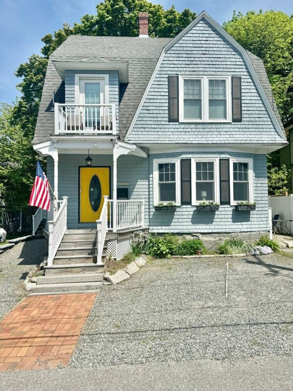 A two-story house with a porch, a yellow door, and an American flag. - The Garden Room at the Lafayette Inn (Bar Harbor)