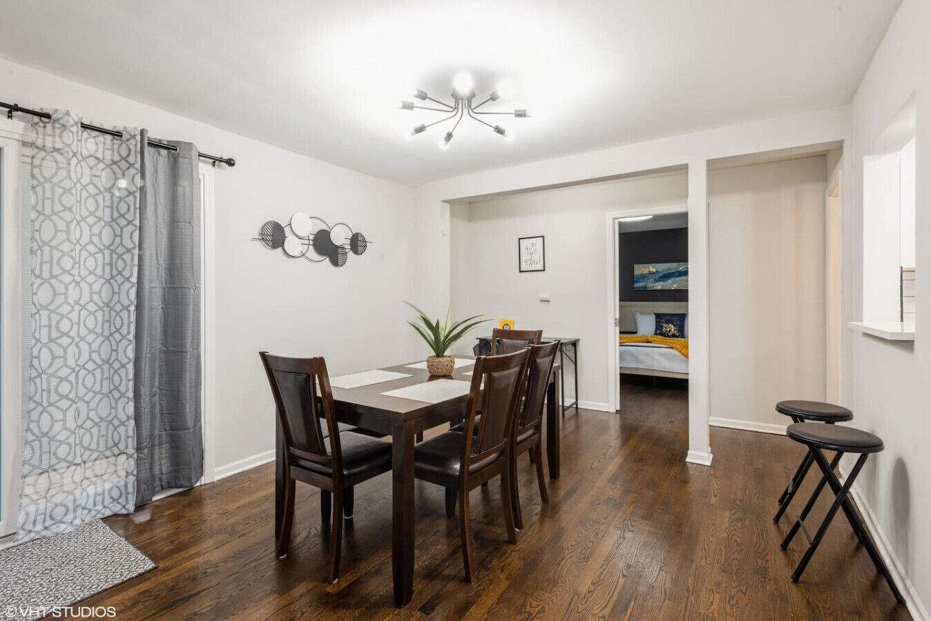 A dining area with a wooden table and chairs, a potted plant, and a modern light fixture.