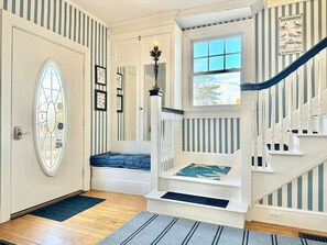 Un escalier avec des rampes blanches et des touches de bleu, une porte ornée d’un vitrail et un mur décoré de tableaux encadrés.