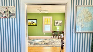 A room with a wooden floor, a dining area with chairs and a table, a ceiling fan, and a window with yellow blinds. - The Cottage Room at Lafayette Inn (Bar Harbor)