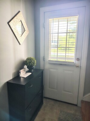 A door with a window, a dark-colored dresser with a plant and a thank you card, and a framed picture on the wall.