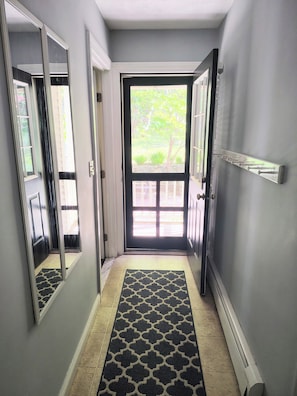 A hallway with a black and white patterned rug, a door leading outside, and a wall-mounted coat rack.