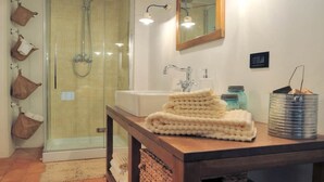 Un baño con ducha de vidrio, tocador de madera con espejo y piso de baldosas.