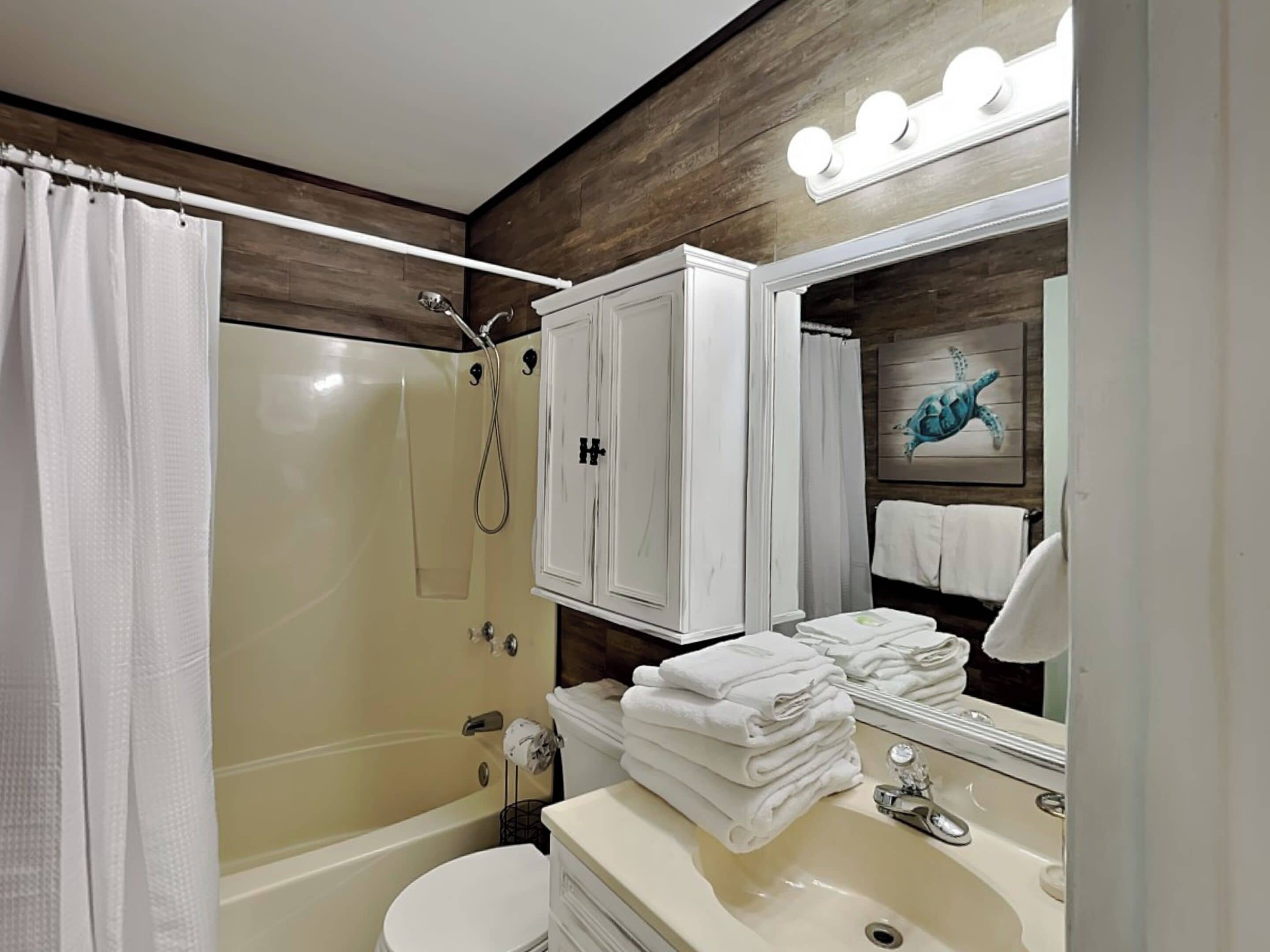 Une salle de bain avec une douche à parois de verre, des toilettes blanches, un lavabo avec un miroir et un porte-serviettes avec des serviettes pliées.
