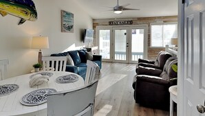Un amplio espacio de sala con una mesa de comedor blanca, un ventilador de techo y un letrero con la inscripción 'STAY SALTY' sobre la entrada.