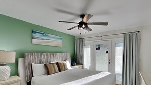 Un dormitorio con cama, mesitas de noche, ventilador de techo, un cuadro y una puerta con cortinas.
