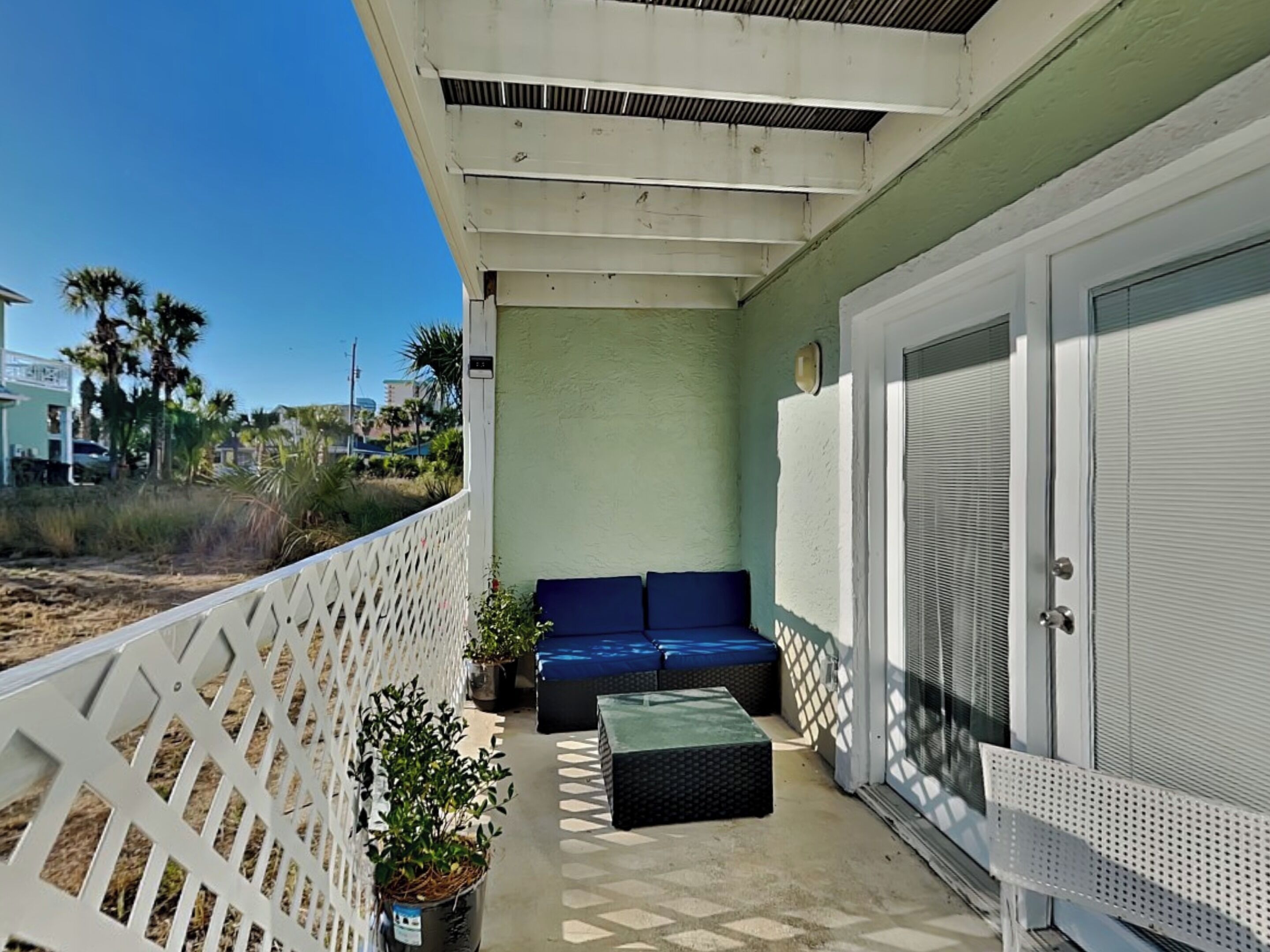 A balcony with a white lattice fence, a blue sofa, a small table, and a potted plant.