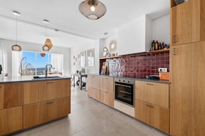 A modern kitchen with wooden cabinets, a tiled backsplash, and pendant lighting.
