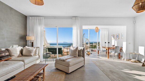 A modern living room with a sofa, a bench, a dining area with chairs, and large windows offering a view of the mountains. - Casa María Luisa: Panoramic Terrace, Spectacular Gibraltar Views & Separate Studio (Manilva)