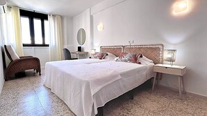 Una cama doble con cabecera trenzada, dos mesitas de noche, una silla, un escritorio y un espejo grande.
