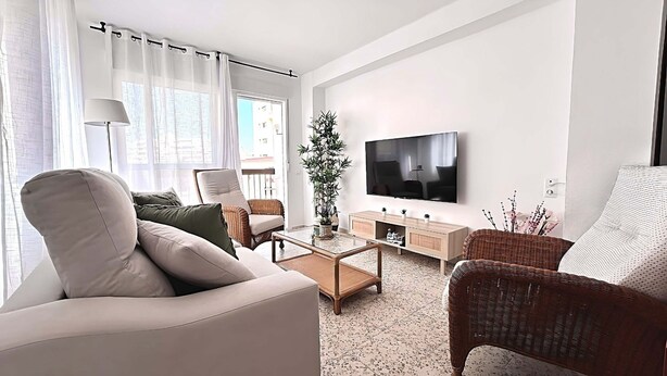 Una sala de estar moderna con un sofá, sillones, una mesa de centro, un televisor y una planta en maceta.