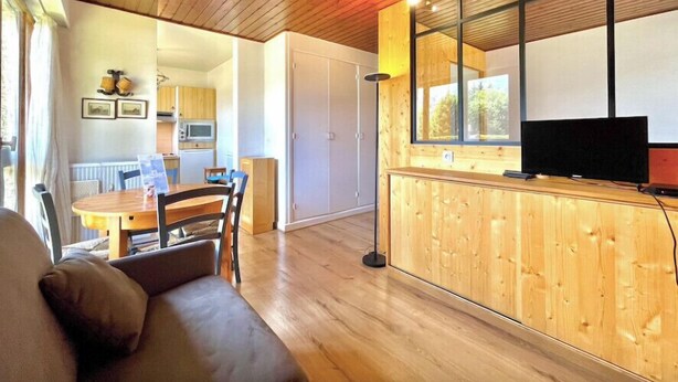 A cozy living room with a wooden ceiling, a dining area with a table and chairs, a kitchen with a microwave, and a TV on a wooden cabinet. - Superb apartment in Megève (Megève)