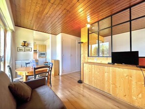A cozy living room with a wooden ceiling, a dining area with a table and chairs, a kitchen with a microwave, and a TV on a wooden cabinet. - Superb apartment in Megève (Megève)