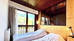 A bedroom with two beds, a window with a view of a mountain, and a wooden ceiling. - Superb apartment in Megève (Megève)