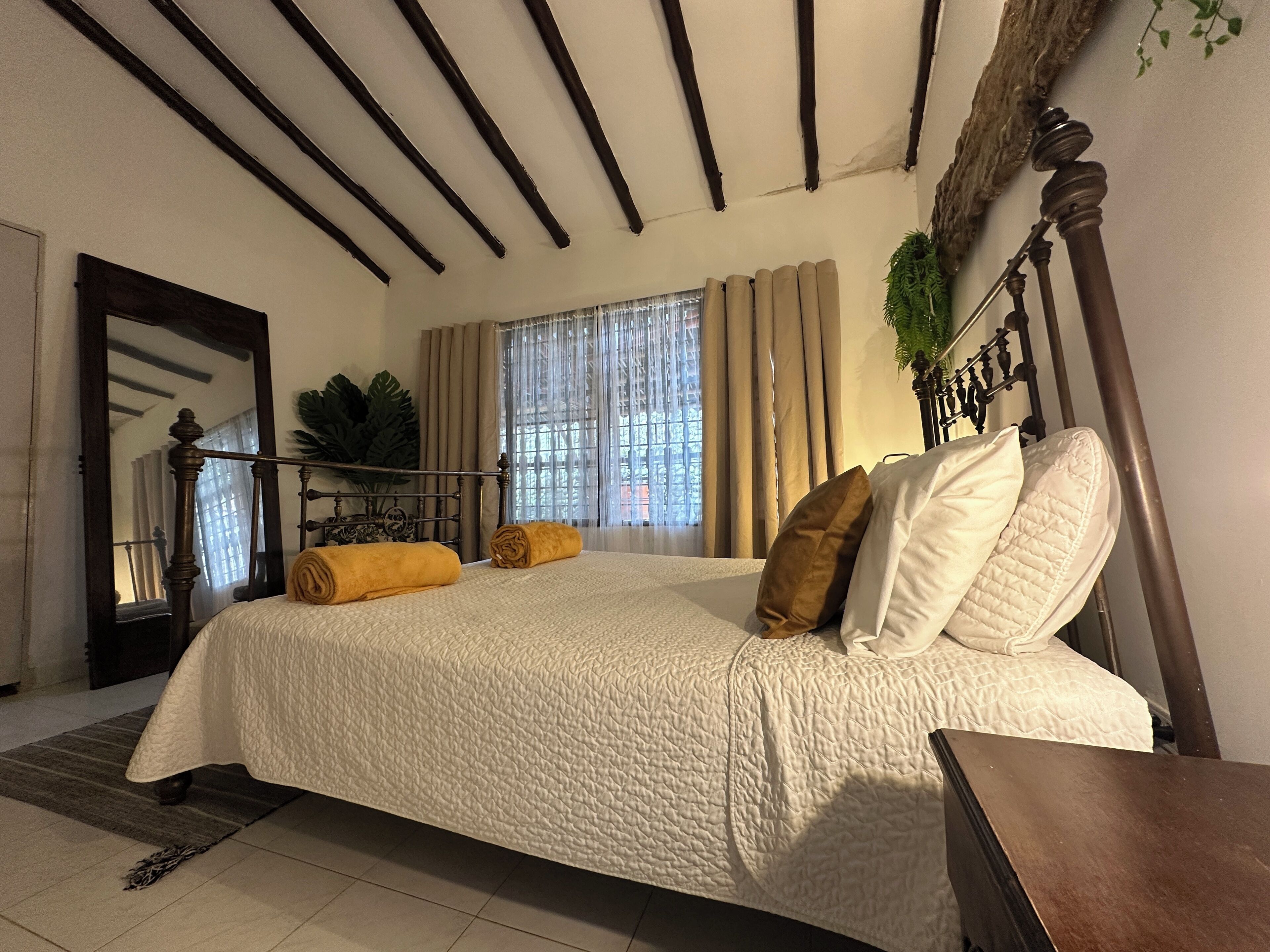 A bedroom with a large bed, a wooden headboard, a mirror, and a window with curtains.