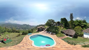 A swimming pool with a tiled deck, surrounded by lush greenery and a mountainous backdrop. - La Villa The View (Cali)