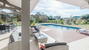 An outdoor patio with a pool, wicker furniture, and a view of the surrounding landscape.