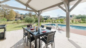 A covered patio with a table set for dining, overlooking a swimming pool and garden.
