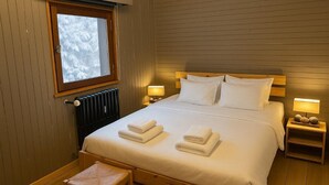 Una cama bien hecha con sábanas y toallas blancas, un cabecero de madera y dos lámparas de noche.
