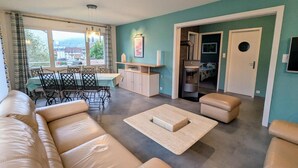 Ein modernes Wohnzimmer mit einer Sofagarnitur, einem Essbereich mit Tisch und Stühlen und Blick ins Freie durch große Fenster.