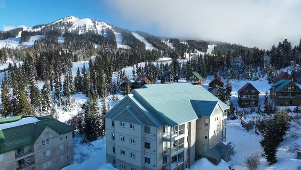 A multi-story hotel with a green roof, surrounded by snow-covered trees and mountains in the background. - Mount Washington’s Mountainside Lodge (Campbell river)