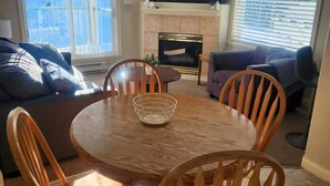 A dining area with a round wooden table and chairs, a fireplace, and a television mounted on the wall. - Mount Washington’s Mountainside Lodge (Campbell river)