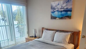 A spacious bedroom with a large bed, a nightstand, a lamp, and a painting on the wall. - Mount Washington’s Mountainside Lodge (Campbell river)
