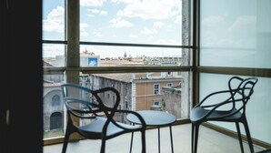 Ein Zimmer mit großem Fenster und Blick auf eine Stadtlandschaft, ausgestattet mit zwei Stühlen und einem Tisch.