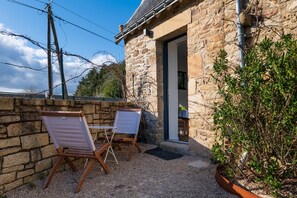 Ein Steinhaus mit einer Tür, einem kleinen Tisch, zwei Stühlen und einem Blumentopf.