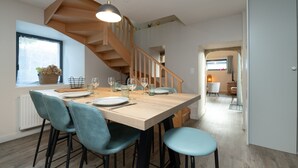 Un coin repas avec une table en bois, des chaises bleues et un escalier.