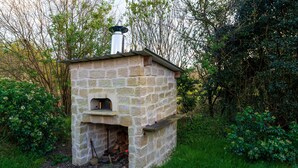 Un four extérieur en pierre, doté d’une cheminée et entouré de verdure.