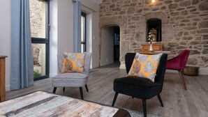 Une pièce avec un mur en pierre, une table en bois, deux chaises dotées de coussins à motifs et une vue dégagée sur l’extérieur grâce à une grande fenêtre.