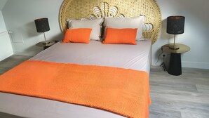 Ein Bett mit einem gewobenen Kopfteil, zwei Nachttischen, zwei Lampen und einer orangefarbenen Tagesdecke.
