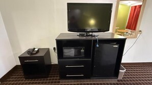 Habitación de hotel con televisión de pantalla plana, microondas, mini refrigerador y una pequeña mesa con un control remoto.