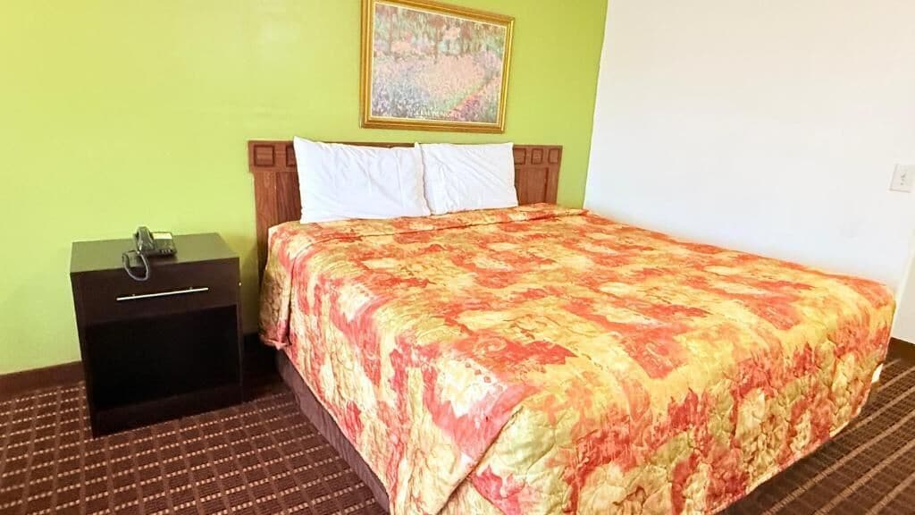 A hotel room with a bed, a nightstand, a telephone, and a painting on the wall.