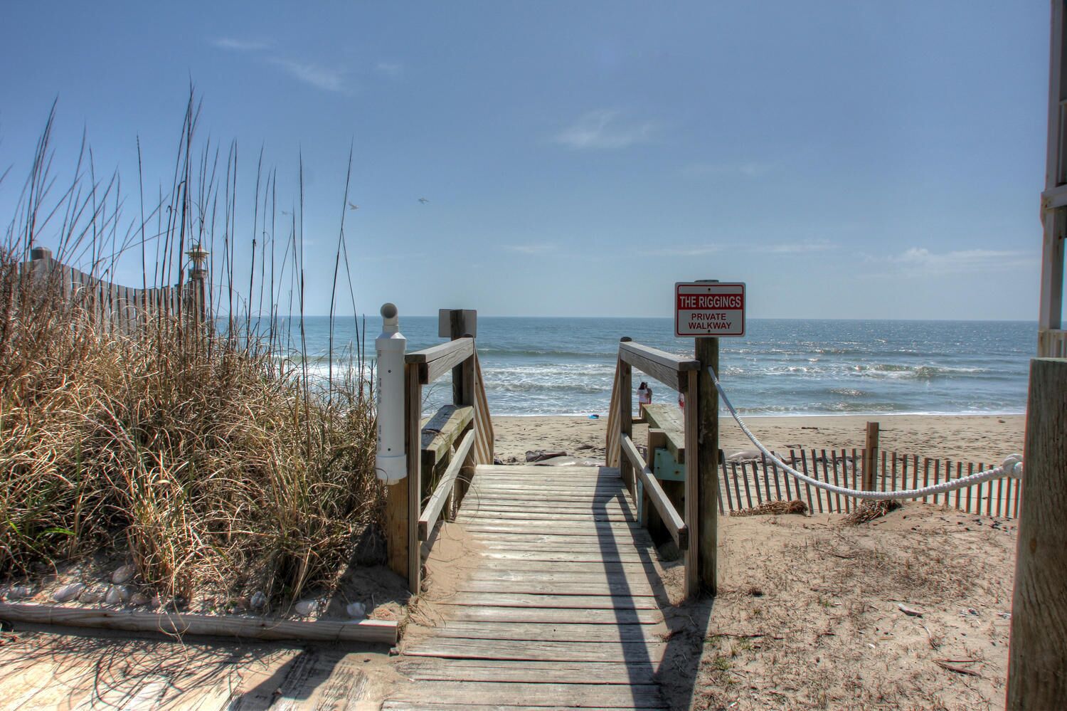 A wooden boardwalk leading to a beach with a sign indicating it is a private walkway.