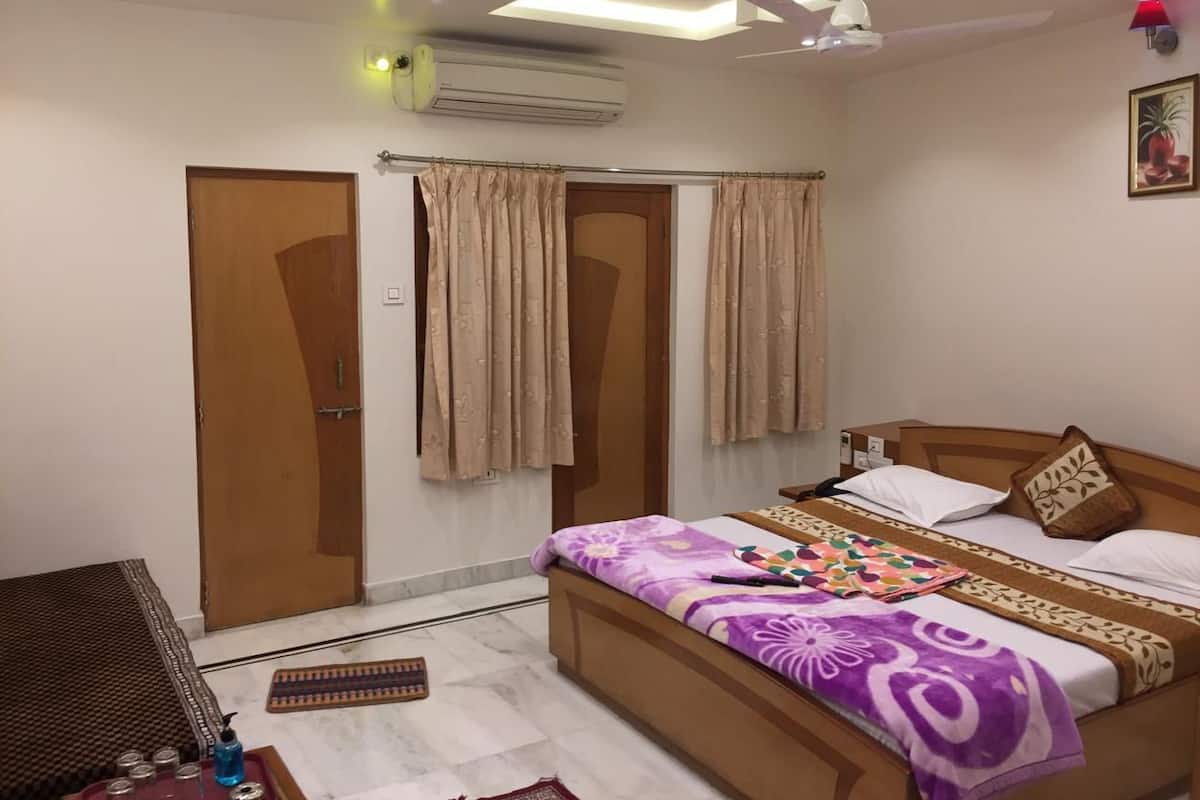 A bedroom with a bed, curtains, an air conditioner, a ceiling fan, and a door.