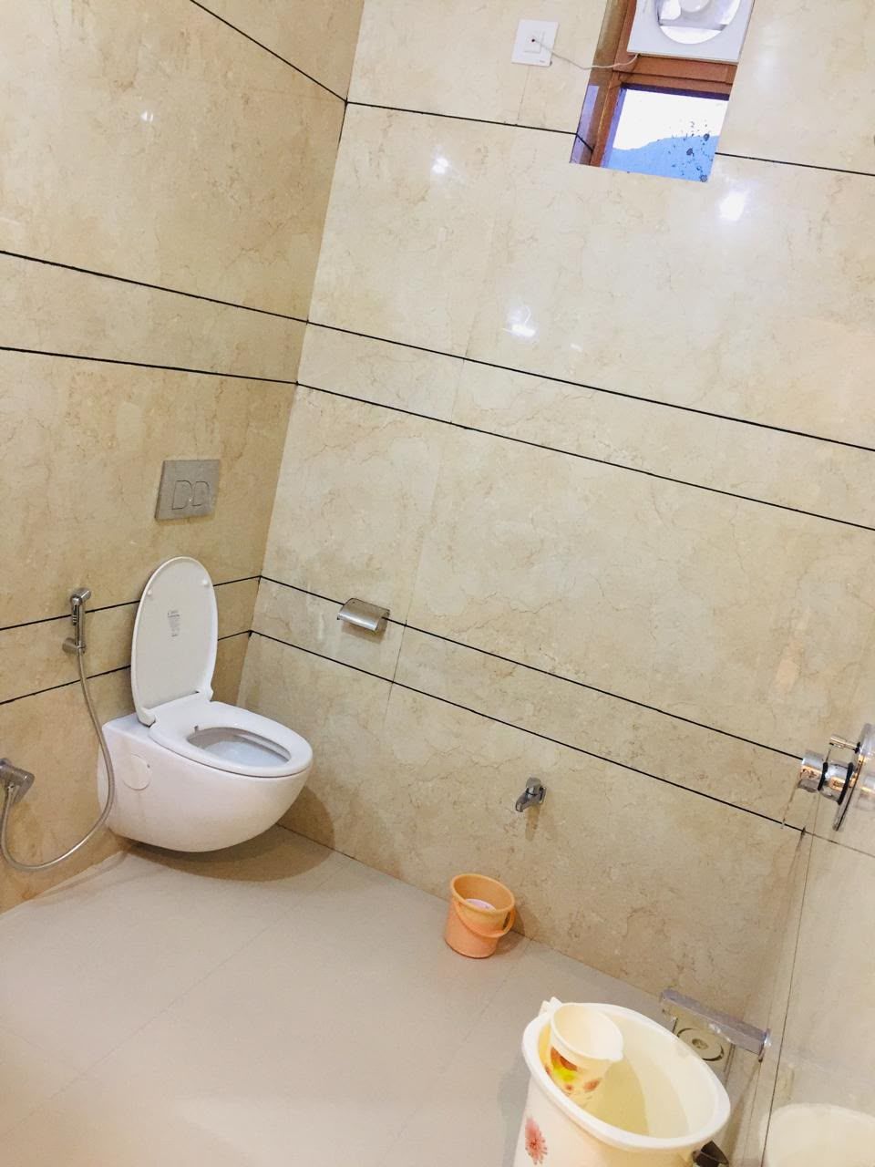 Een badkamer met een toilet, een klein wastafeltje en een emmer.