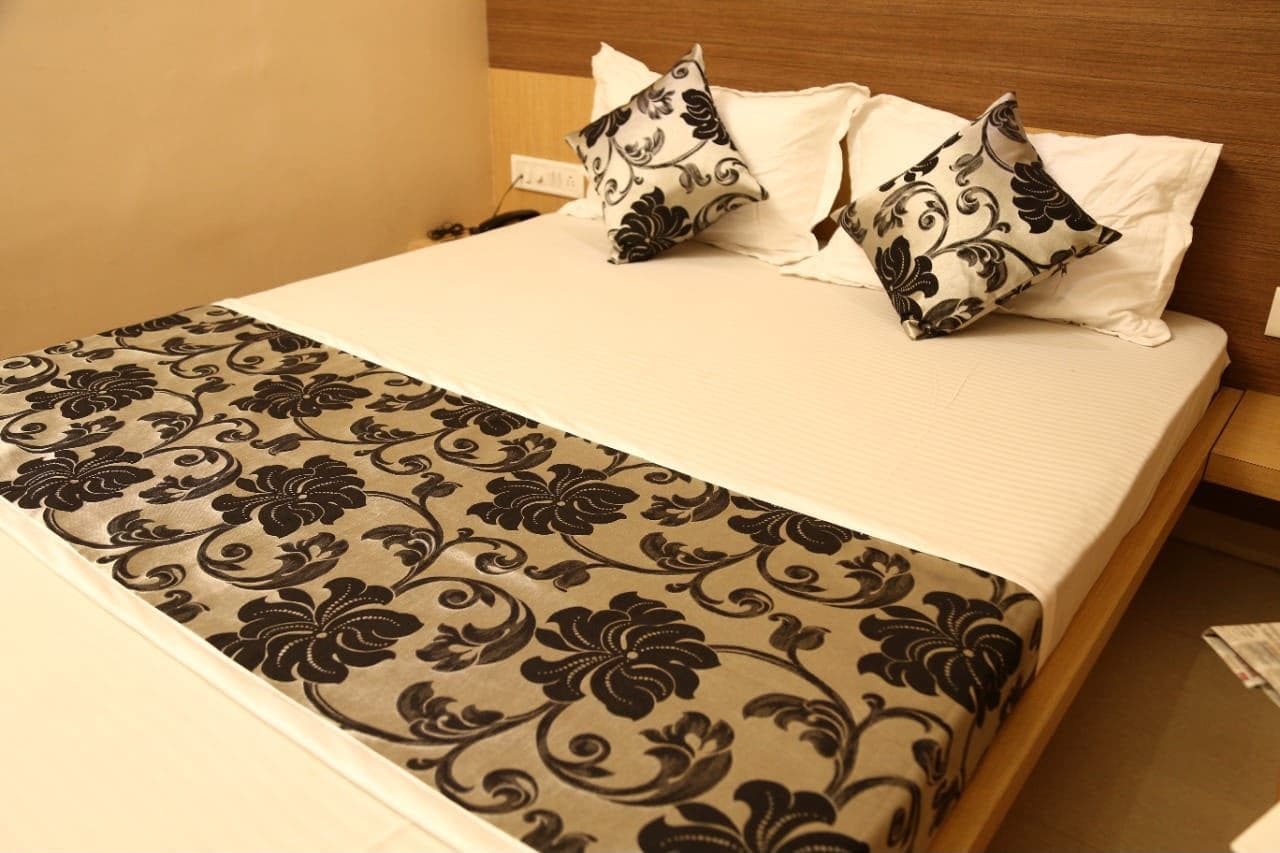 A hotel room with a bed, white bedding, a patterned throw blanket, and decorative pillows.