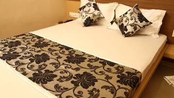 Una habitación de hotel con cama, ropa de cama blanca, una manta con estampado y almohadas decorativas.